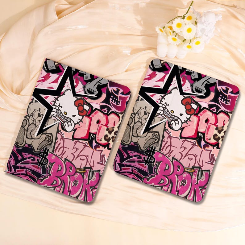 May include: Two rectangular cases with a graffiti-style design. The cases feature a pink, black, and grey colour scheme with a cartoon cat character, stars, and the word "BROK" in pink graffiti lettering.