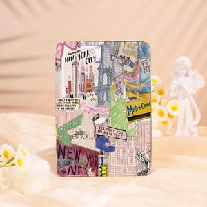 May include: A rectangular design with a collage of New York City imagery, including the Statue of Liberty, a yellow taxi, and the Brooklyn Bridge. Text elements include "New York City", "Broadway", and "I'll meet you in New York".
