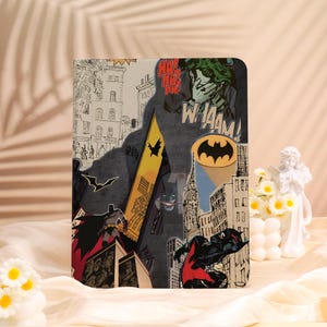 May include: A Batman-themed tablet case featuring comic book-style illustrations. The design includes the Batman logo, the Joker, and cityscape elements. The case is primarily gray, with accents of yellow, black, and red.