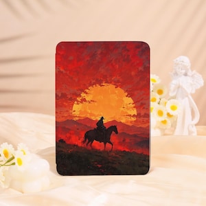 May include: A black tablet case featuring a cowboy on horseback silhouetted against a fiery sunset. The artwork depicts a dramatic scene with a large orange sun, mountains, and a red sky, creating a Western theme.