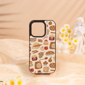 May include: A phone case with a black border and a repeating pattern of baking-related illustrations. The design includes images of bread, apples, flour sacks, rolling pins, and jam jars. The case has a cutout for the camera and flash.