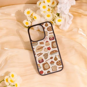 May include: A phone case with a black border and a white background featuring a repeating pattern of baked goods. The design includes illustrations of bread, apples, cinnamon rolls, and jars of jam.