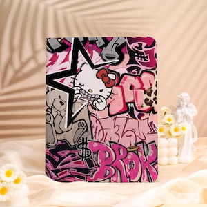 May include: A colorful tablet case featuring a graffiti-style design. The artwork includes a star, a cartoon cat character, and various graffiti tags in shades of pink, black, and white. A dollar sign is also visible.
