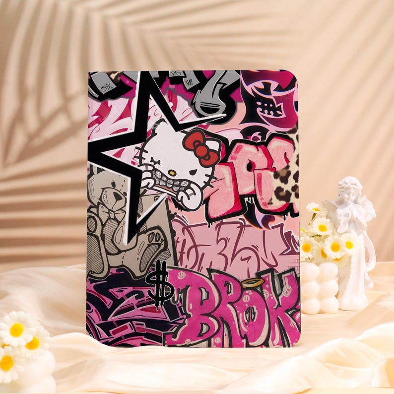 May include: A tablet case with a vibrant graffiti design. The artwork incorporates a star, a cartoon cat character, and graffiti tags in pink, black, and white. A dollar sign is also included in the design.