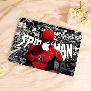 May include: A rectangular laptop skin featuring a vibrant illustration of Spider-Man in a red and black suit. The background is a collage of comic book panels in black, white, and gray, with the words "SPIDER-MAN" prominently displayed.