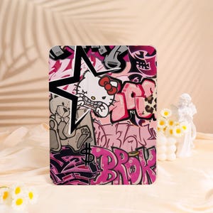 May include: A tablet case with a graffiti design, including a star, a teddy bear, and a Hello Kitty character. The case is in pink, black, and white, with the word "BROK" in pink graffiti lettering.