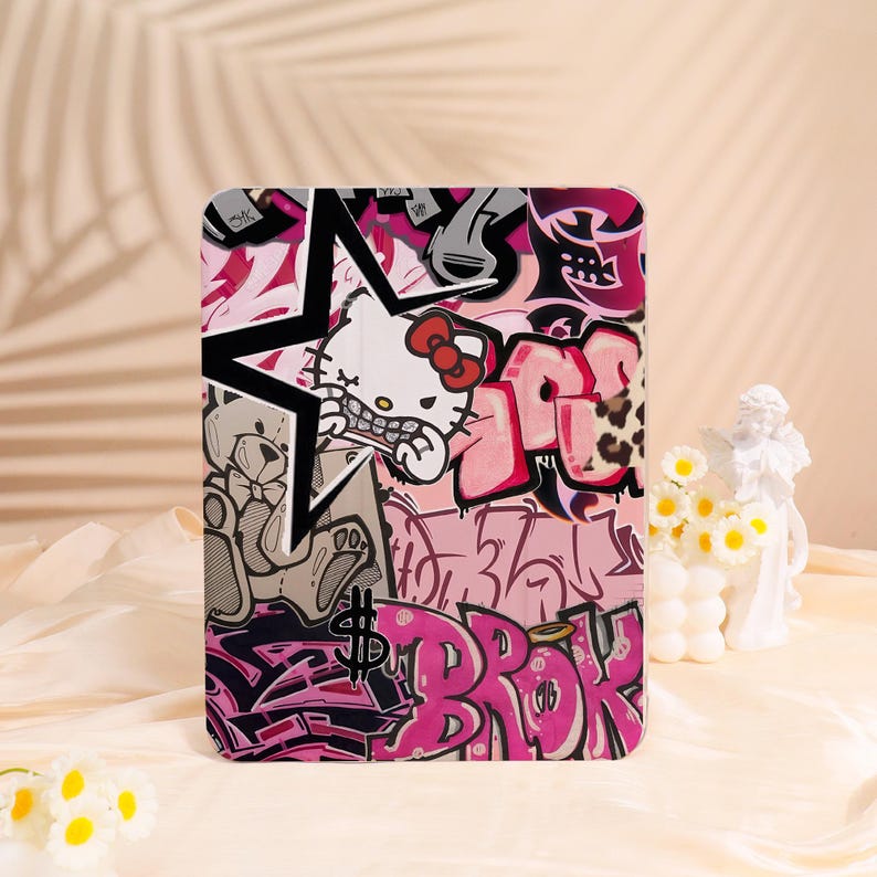 May include: A tablet case with a graffiti design, including a star, a teddy bear, and a Hello Kitty character. The case is in pink, black, and white, with the word "BROK" in pink graffiti lettering.