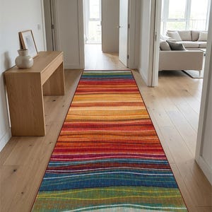 May include: A long rectangular runner rug featuring a horizontal striped pattern with a vibrant gradient of colours including red, orange, yellow, blue, and green. The rug has a thin dark red border and a textured appearance throughout the surface.