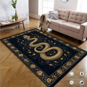 Op de afbeelding: Zwart en gouden vloerkleed met een gedetailleerde illustratie van een slang die om een ​​bloemmotief is gewikkeld. Het vloerkleed heeft een zwarte achtergrond met een gouden rand.