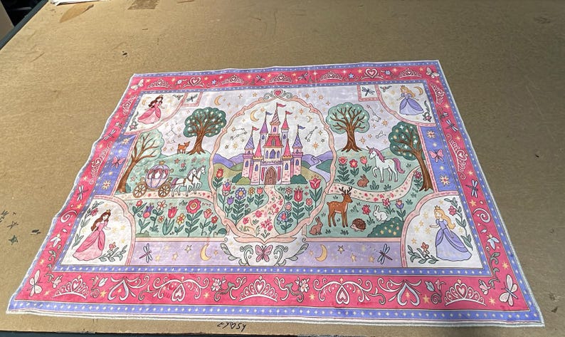 Peut inclure: Un panneau de tissu rectangulaire pr&eacute;sentant un ch&acirc;teau rose central entour&eacute; d'un jardin avec une licorne, un cerf, un lapin et un h&eacute;risson. La sc&egrave;ne comprend une cal&egrave;che, des arbres et quatre personnages en robe, encadr&eacute;s par une bordure florale rose.