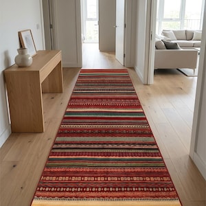 May include: A long rectangular runner rug featuring a vibrant pattern of horizontal stripes in shades of red, green, blue, and cream. The design incorporates various geometric motifs, including small squares, dots, and zigzags, spanning the entire length.