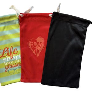 May include: Three different eyeglass cases. One is black, one is red with the words "peace love" in a heart shape, and one is blue and yellow striped with the words "Life is short buy the glasses".