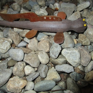 May include: A metal sculpture of a fish with brown and orange accents. The fish is lying on a bed of gray and brown rocks.