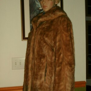 May include: A brown fur coat with a high collar and a matching brown fur hat. The coat is worn by a mannequin with blonde hair.