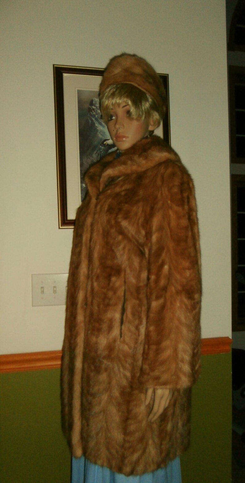 May include: A brown fur coat with a high collar and a matching brown fur hat. The coat is worn by a mannequin with blonde hair.