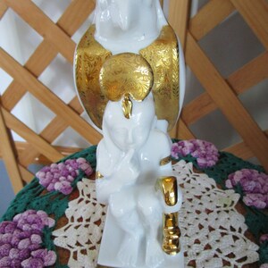 May include: White porcelain figurine of a seated figure with a gold owl perched on its shoulders. The owl has gold accents and the figure has a gold band around its wrist. The figurine is sitting on a gold base.