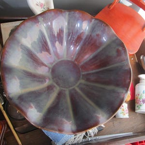 May include: A large, brown ceramic bowl with a scalloped edge and a white and purple glaze. The bowl has a unique, flower-like design.