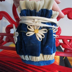 May include: A blue velvet pouch with white lace trim and white daisy embellishments. The pouch is tied with a white ribbon.