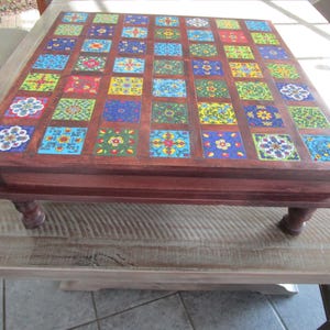 May include: A wooden coffee table with a square top inlaid with colorful tiles. The tiles are arranged in a grid pattern and feature floral designs. The table has four turned legs.