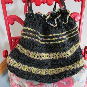 May include: A black crocheted drawstring bag with colorful stripes and a ruffled top. The bag is hanging on a red metal hook.