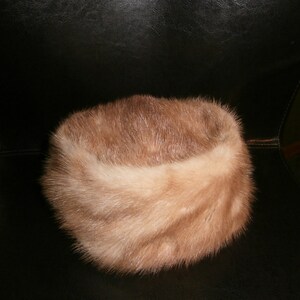 May include: A light brown fur hat with a wide brim. The hat is made of soft, fluffy fur and has a simple, classic design.