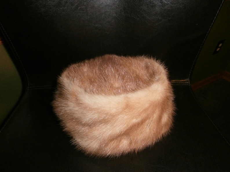 May include: A light brown fur hat with a wide brim. The hat is made of soft, fluffy fur and has a simple, classic design.