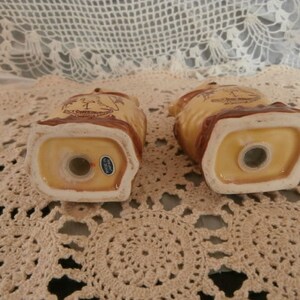 May include: A pair of ceramic owl-shaped salt and pepper shakers. The shakers are tan with brown detailing and a white rim. Each has a dispensing hole and a small sticker reading "Made in Japan".