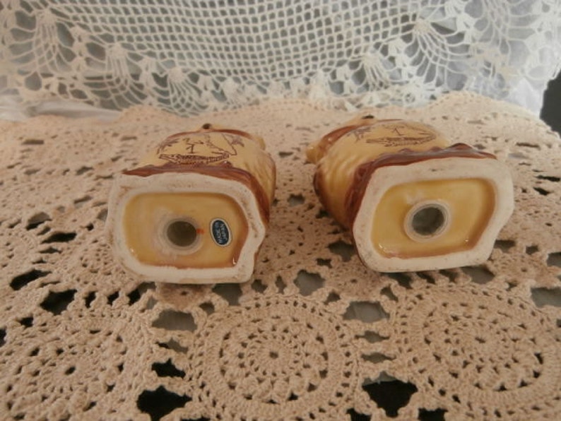 May include: A pair of ceramic owl-shaped salt and pepper shakers. The shakers are tan with brown detailing and a white rim. Each has a dispensing hole and a small sticker reading "Made in Japan".