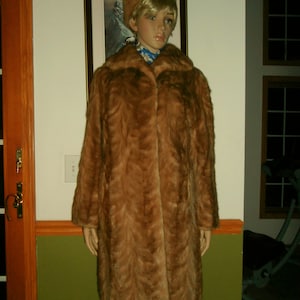 May include: A brown fur coat with a long, straight cut. The coat has a collar and a button closure. The fur is soft and fluffy.