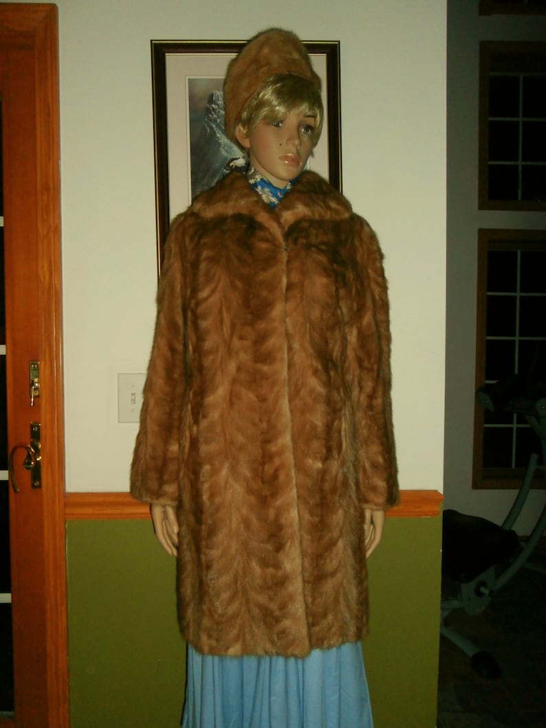 May include: A brown fur coat with a long, straight cut. The coat has a collar and a button closure. The fur is soft and fluffy.
