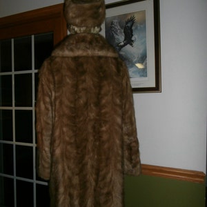 May include: A brown fur coat with a matching brown fur hat. The coat is long and has a collar. The hat is a cloche style.