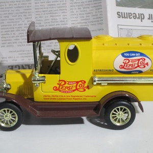 May include: A yellow toy truck with a brown cab and a Pepsi-Cola logo on the side. The truck has a gold-colored gas tank and wheels. The text on the side reads "Drink Pepsi-Cola Delicious. Pepsi, Pepsi-Cola are registered trademarks. Used under license from PepsiCo, Inc."