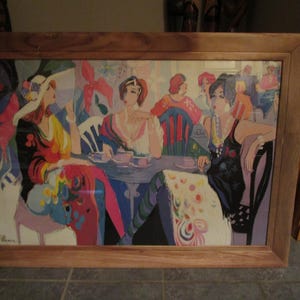 May include: A framed print of a colorful painting depicting four women sitting at a table. The women are wearing vibrant clothing and have unique hairstyles. The painting is set in a cafe or restaurant setting with a table and chairs. The print is framed in a wooden frame.