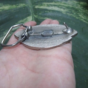 Puede incluir: Hebilla de cintur&oacute;n plateada con un dise&ntilde;o detallado de una hoja. La hebilla tiene un cierre de gancho y un acabado liso y pulido.