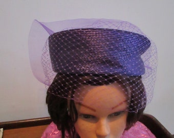 May include: A purple straw hat with a matching purple veil. The hat has a wide brim and a rounded crown.