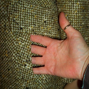 Puede incluir: Primer plano de una tela de tweed marr&oacute;n con un bolsillo. La tela tiene un sutil patr&oacute;n de motas amarillas y negras.