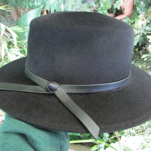 May include: A black felt fedora hat with a wide brim and a black leather band around the crown. The band has a bow at the front.