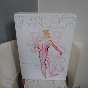 May include: A pink and white box with the text "Classique Collection" and "Evening Elegance Barbie" on the front. The box features a drawing of a Barbie doll wearing a pink and white gown with a large pink flower.