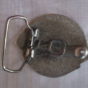 Puede incluir: Hebilla de cintur&oacute;n de plata con un dise&ntilde;o detallado y un lazo de plata. La hebilla tiene una peque&ntilde;a etiqueta de metal con el n&uacute;mero "101" en ella.