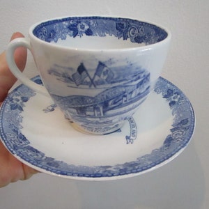 May include: A blue and white teacup and saucer set with a floral design and a scene of a bridge with flags. The saucer has the words "Old England" on it.