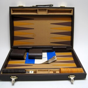 May include: Open backgammon set in a brown leather case. The game board features brown and yellow triangles. Accessories include dice, dice cups, and playing pieces. The case is open, revealing the game components.