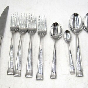 May include: A collection of stainless steel silverware, including knives, forks, and spoons. The set features a polished finish, with a simple, elegant design. The knives, forks, and spoons are arranged on a white surface.