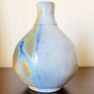 May include: A small, round ceramic vase with a narrow neck. The vase is decorated with a blue, green, and brown glaze.