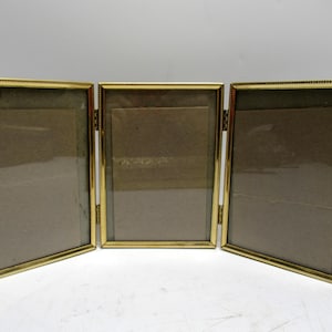 May include: A gold-colored, three-panel photo frame. Each panel has a rectangular opening for a photo, with a clear glass cover. The frame has a decorative beaded edge and is hinged to fold.