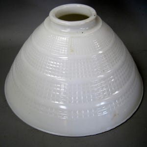 May include: A white milk glass lamp shade with a conical shape and a tiered design. The surface features a repeating grid pattern of small squares embossed into the glass. The shade has a circular opening at the top and a wide, flared base.