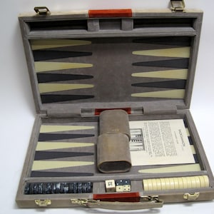 May include: Open backgammon set in a gray case with black, cream, and gray game pieces. The case has a red handle and trim. Includes dice, dice cups, and a game instruction sheet.