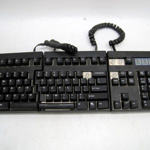 May include: A black, split keyboard with a numeric keypad and a coiled cord. The keyboard has three sections, with the center section labeled "IMPORTANT". The keys are black with white lettering.