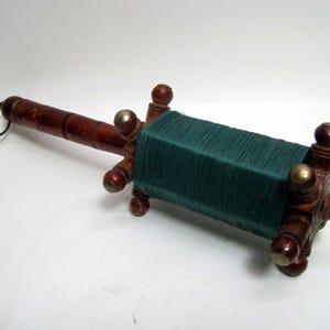May include: A wooden spool with a green string wrapped around it. The spool has a handle and a metal ring on one end. It is a traditional toy used for playing kite.