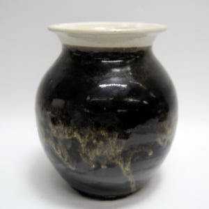 May include: A small, round ceramic vase with a dark brown glaze and a white rim. The glaze has a mottled appearance with lighter brown streaks.