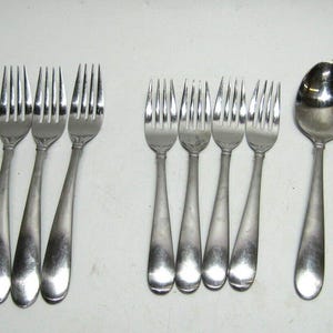 May include: A set of silverware, including forks, knives, and a spoon, all made of stainless steel. The silverware has a simple, elegant design with rounded handles.